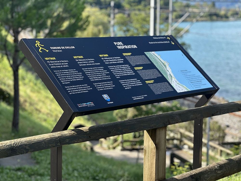 Pupitre d'orientation trilingue « Parking de Chillon », face au lac Léman, avec son plan de situation et le pictogramme jaune du piéton
