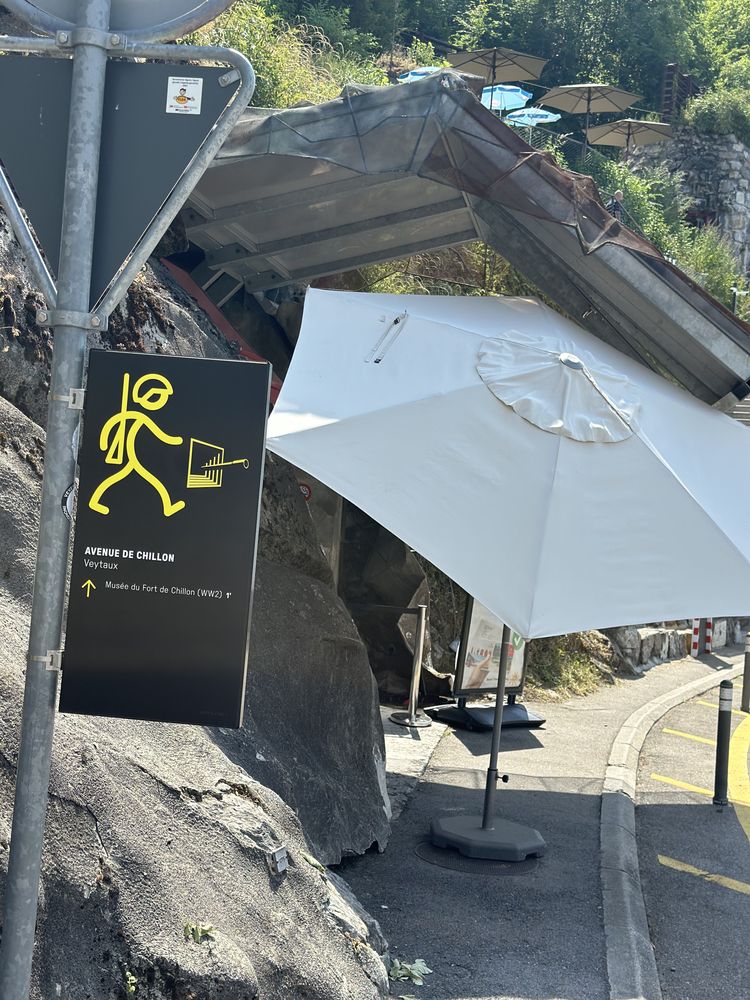 Indicateur directionnel de l'avenue de Chillon vers le Musée du Fort de Chillon, pictogramme jaune sur fond noir, adossé au rocher