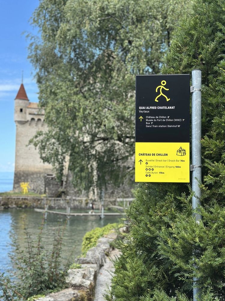 Mât directionnel du quai Alfred-Chatelanat à Veytaux, panneau noir et bandeau jaune, avec le château de Chillon en arrière-plan